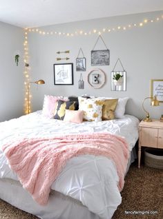 a white bed topped with pink blankets and pillows next to a wall filled with pictures