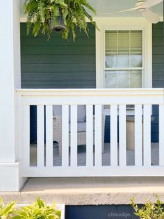 the front porch of a house with white railings and green plants hanging from it