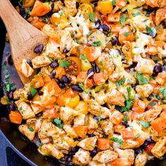 a skillet filled with chicken, black beans and carrots next to a wooden spoon