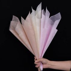 a hand holding several folded paper flowers on a black background in the shape of an umbrella