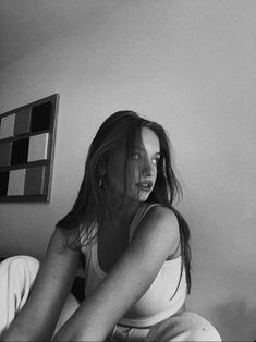 a black and white photo of a woman sitting on a bed with her hair blowing in the wind