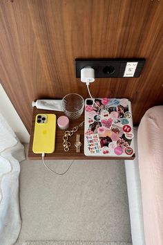 a wooden table topped with a phone and other items on top of it next to a bed