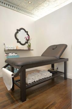 a massage table in a room with wood floors and white walls, along with towels on the shelf