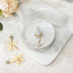 a white plate topped with a gold ring next to flowers