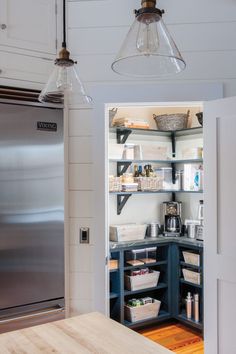 an open pantry in the corner of a kitchen with stainless steel refrigerator and wooden table