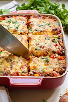 a person cutting into a lasagna casserole in a red dish with a spatula