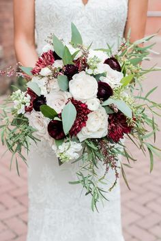 a bridal holding a bouquet of flowers and greenery in her hands on a brick walkway