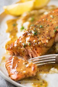 a piece of salmon covered in gravy with lemon wedges