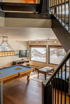 a pool table sitting in the middle of a living room next to a stair case