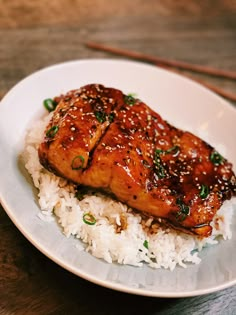 a white plate topped with rice and meat next to chopsticks on a wooden table