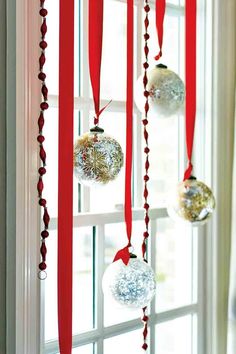 some ornaments hanging from a window in front of a red ribbon and white glass ornament