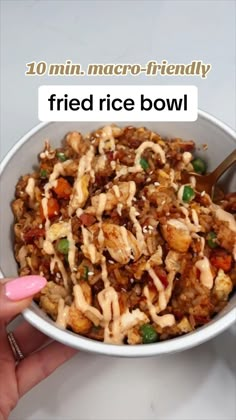 a person holding a spoon in a bowl filled with fried rice and veggies