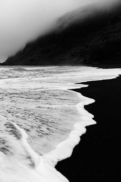 a black and white photo of the ocean with waves crashing on it's shore