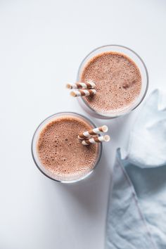 two glasses filled with chocolate milkshakes sitting on top of a white countertop