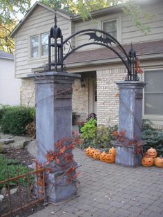 two metal pillars with pumpkins on them in front of a house and gated yard