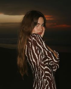 a woman with long hair standing in front of the sun at night wearing a zebra print jacket