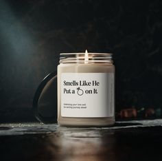 a candle sitting on top of a wooden table next to a black mug with the words smells like he pua o'n it