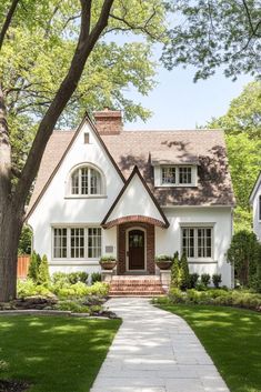 a white house with trees and grass in the front yard, along with a walkway leading up to it