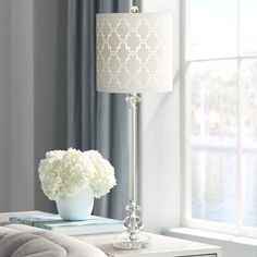 a white table lamp sitting on top of a dresser next to a vase filled with flowers