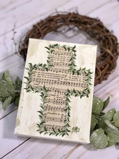 a cross made out of sheet music sits next to a wreath on a white wooden surface