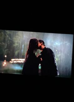 two people are kissing in the rain on a television screen with lights shining down behind them