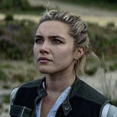 a close up of a person wearing a jacket and looking off to the side with trees in the background