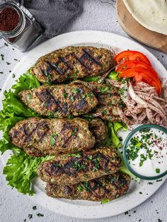 some meat patties are on a plate with lettuce, tomatoes and sauce