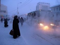 people walking in the snow near buses and cars on a snowy street with buildings behind them