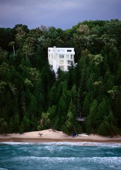 a white house sitting on top of a lush green forest covered hillside next to the ocean