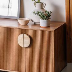 a wooden cabinet with a vase on top and a small plant in the bowl next to it