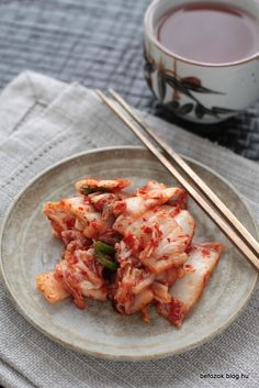 some food on a plate with chopsticks and a cup of tea next to it