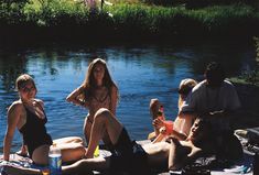 a group of people sitting on top of a blanket next to a river