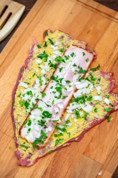 a wooden cutting board topped with meat covered in cheese and parsley next to utensils