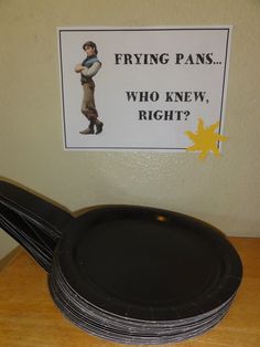 a stack of black paper plates sitting on top of a wooden table next to a sign that says frying pans who knew right?