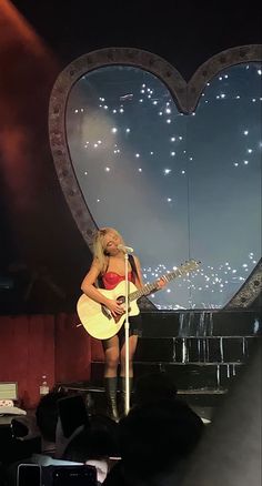 a woman with a guitar on stage in front of a heart shaped window at night