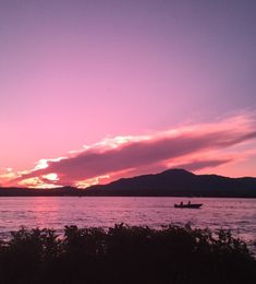 the sun is setting over the water and mountains in the distance, with a boat out on the water