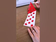 someone is making a card with red polka dots on white paper and holding it in their hand