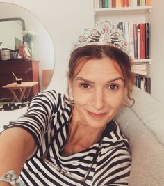 a woman wearing a tiara sitting on a couch in front of a bookshelf