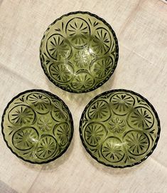 three green bowls sitting on top of a white cloth covered table next to each other