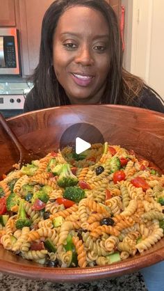 a woman holding up a large wooden bowl filled with pasta and vegtables