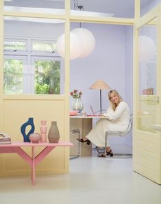 a woman sitting at a pink table in a room with yellow walls and white floors