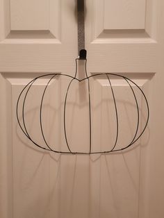 a white door with a wire pumpkin hanging from it's side and a black hook in the middle