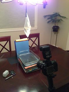 a table with a camera, laptop and other items on it in front of a window