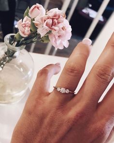 a woman's hand with a diamond ring on it next to a flower vase