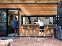 two people standing at a bar in front of a wooden building with sliding glass doors