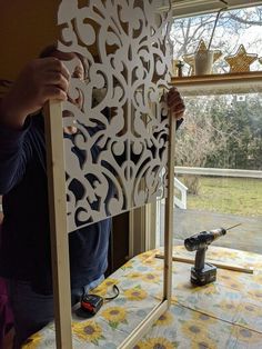 a man is working on an intricate cutout in front of a window with a driller