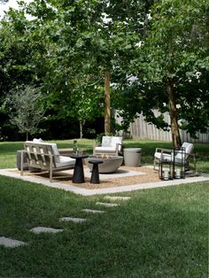 an outdoor living area with couches, tables and chairs in the grass next to trees