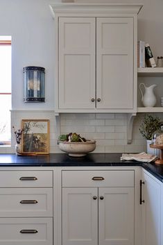 a kitchen with white cabinets and black counter tops in front of an open window on the wall