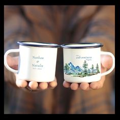 two people holding coffee mugs with mountains and trees painted on the cups in their hands