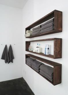 two wooden shelves with towels on them in a white walled bathroom, along with towel racks